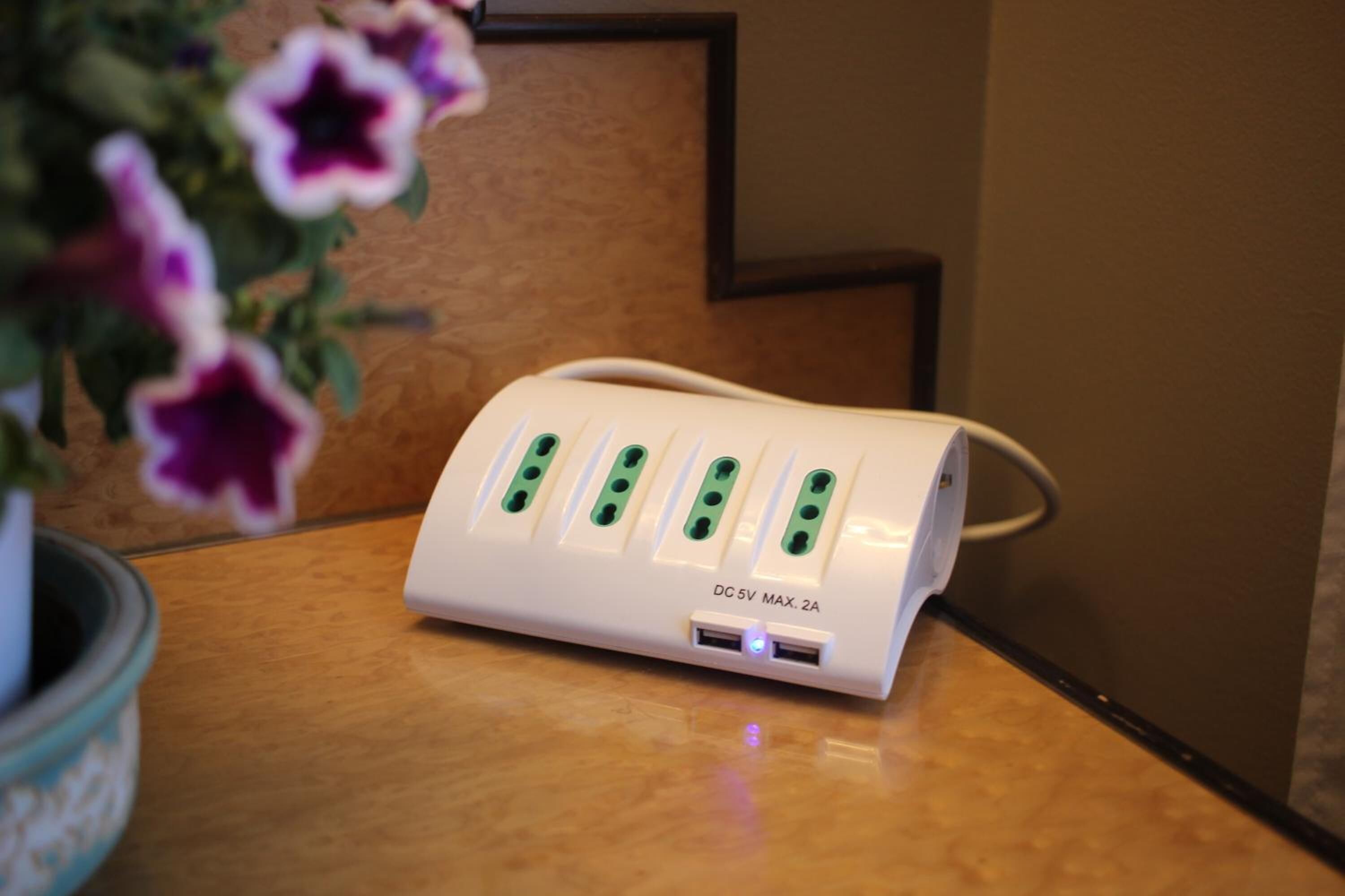 A white power strip with five USB ports and a label reading "DC 5V MAX. 2A" on a wooden surface.