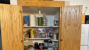Een houten kast met planken vol diverse etenswaren, een koffiezetapparaat en een blender.