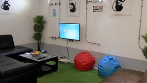 Zona d'estar moderna amb un sofà negre, un seient de plomes vermell i blau, una taula petita amb un bol de fruita i un televisor de pantalla plana muntat a la paret.