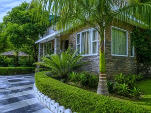 A modern house with stone walls, large windows, and a well-maintained garden with palm trees and hedges. - Park Exotica Resort & Spa - Near Fateh Sagar Lake, Udaipur (Udaipur)