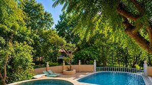 Un espace piscine avec deux jacuzzis, entouré d’une végétation luxuriante, et un bâtiment en arrière-plan.