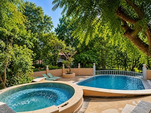 Un espace piscine avec deux jacuzzis, entouré d’une végétation luxuriante, et un bâtiment en arrière-plan.