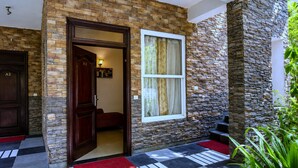 Une entrée moderne, avec une façade en pierre, une porte en bois portant l’inscription « A1 » et un paillasson rouge menant à un hall d’entrée carrelé.