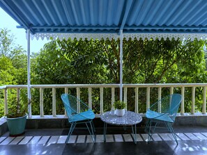 A covered outdoor seating area with two chairs and a table, surrounded by a white railing and lush greenery.