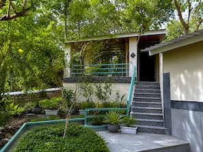 A building with a staircase leading to a door, surrounded by greenery and potted plants.