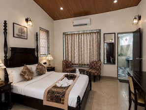 A hotel room with a bed, two chairs, a desk, a mirror, and a window with curtains.