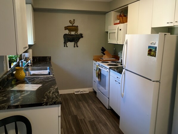 A compact kitchen with white cabinets, a microwave, a stove, and a refrigerator. - Cozy Gem in heart of historic Livingston, Montana (Livingston)