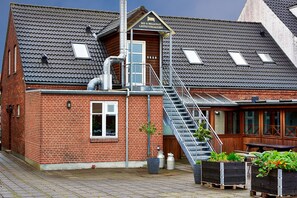 A brick building with a wooden exterior, a staircase leading to a door labeled "BED & BREAKFAST GESTIGGIVERGAARDEN," and outdoor seating with planters. - Bed and Breakfast Phønix (Holstebro)