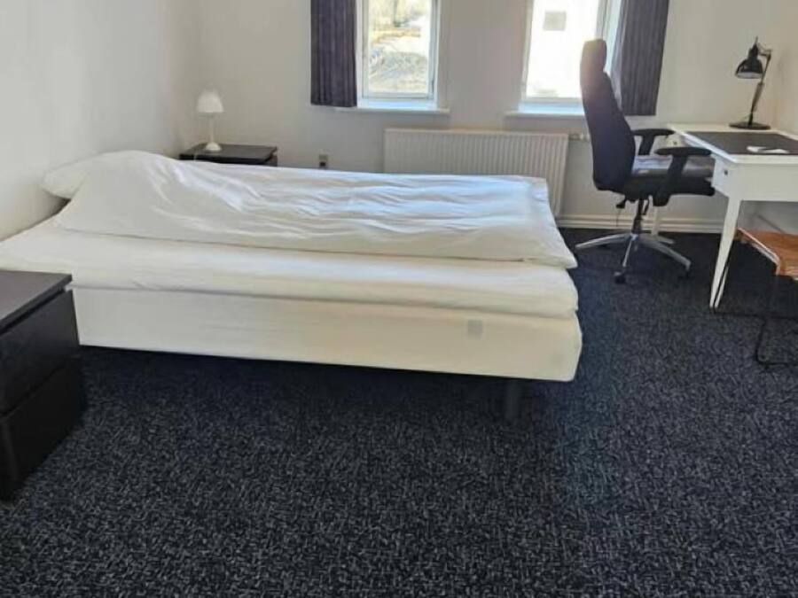 Una habitación de hotel con una cama, un escritorio, una silla y dos ventanas.