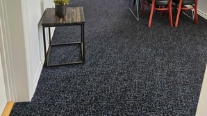 Ein schmaler Flur mit dunklem Teppich führt zu einem Essbereich mit Tisch und Stühlen, einem Sofa und einem an der Wand befestigten Fernseher.