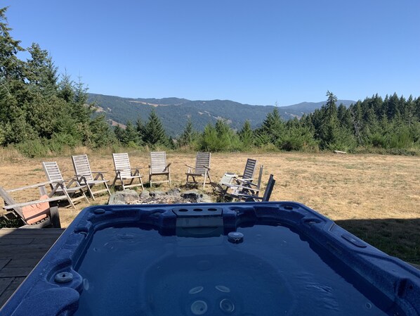 Un jacuzzi con vistas a montañas y un espacio verde con sillas.