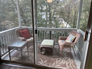 Relax in this serene outdoor space with a comfortable seating area featuring two wicker chairs and a small ottoman.