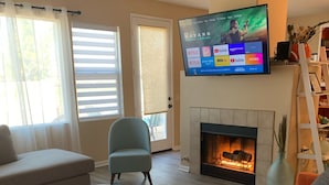 A living room with a fireplace, a flat-screen TV mounted above it, and a comfortable seating area with a sofa and armchairs.