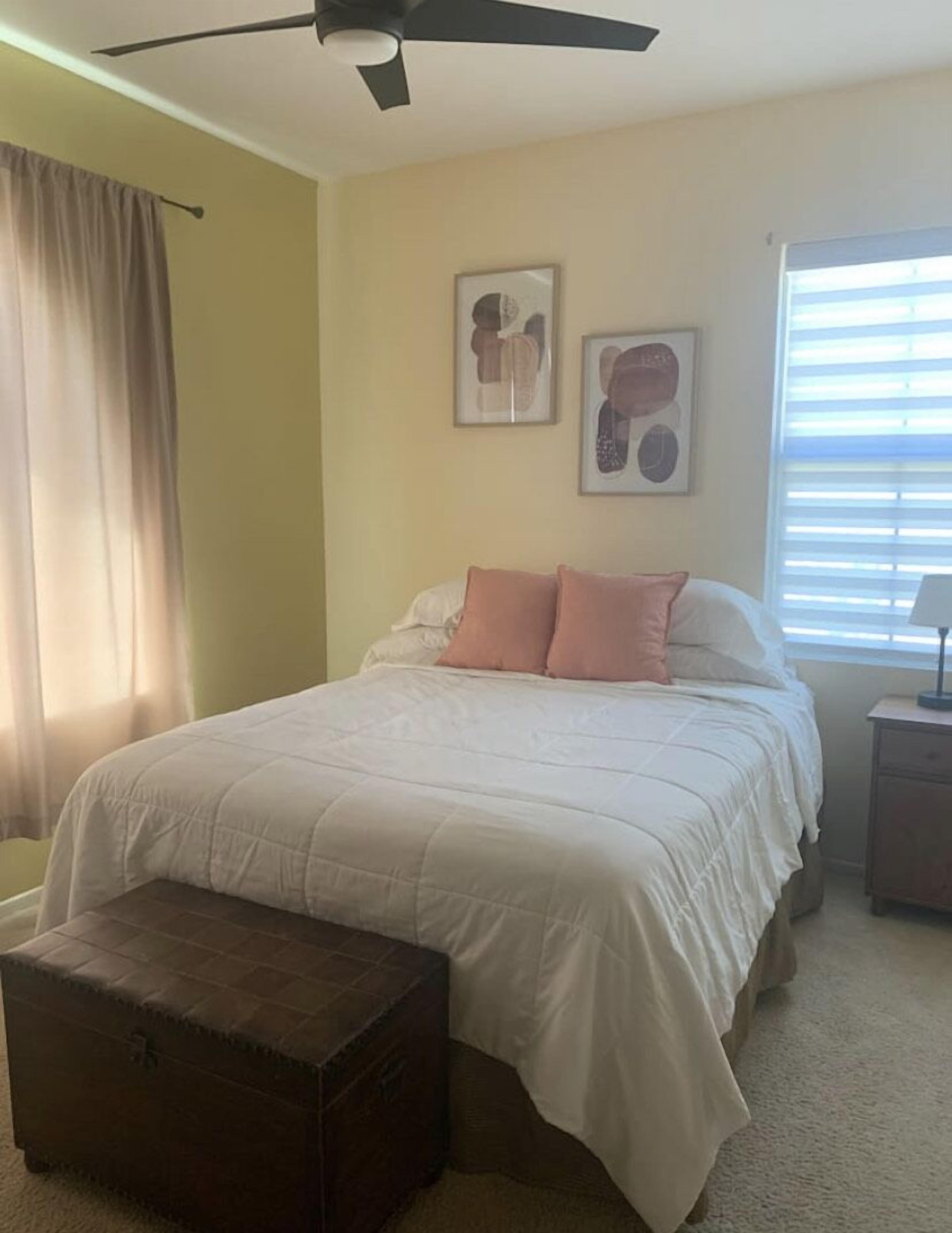 Ein Schlafzimmer mit einem Bett, einer Kommode, einem Deckenventilator und zwei gerahmten Bildern an der Wand.