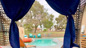 A poolside lounge area with a blue cushioned seating arrangement, a pool, and a view of the surrounding area.