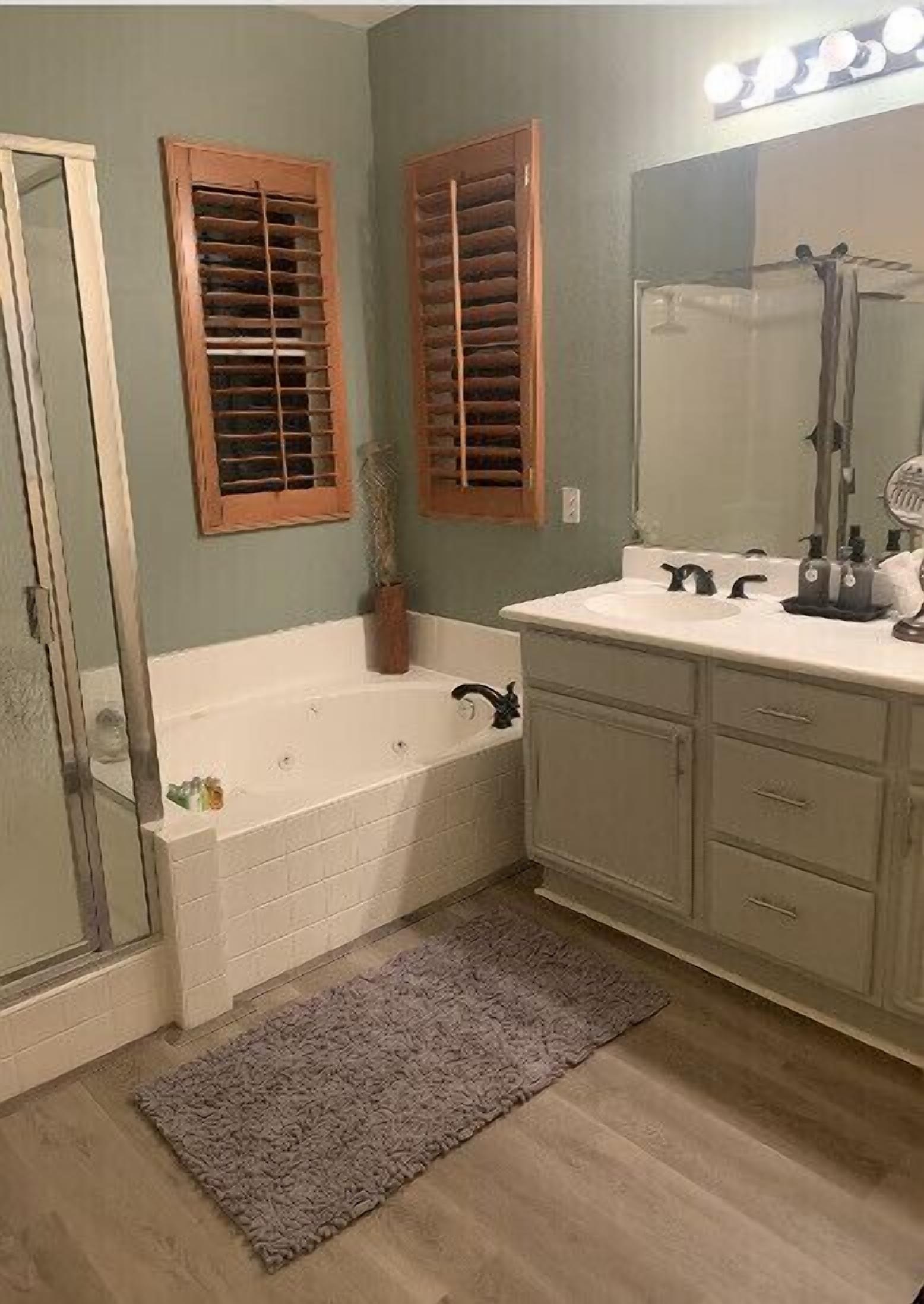 A bathroom with a bathtub, a shower, a vanity with a mirror, and wooden window shutters.