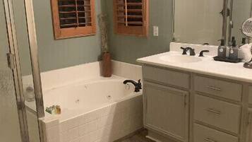 A bathroom with a bathtub, a shower, a vanity with a mirror, and wooden window shutters.