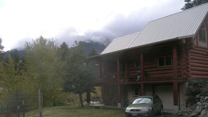 A log cabin with a car parked in front, surrounded by trees and mountains. - Log cabin for salmon, fishing, hiking, cross-country skiing, 50 minutes to ski (Pollock)
