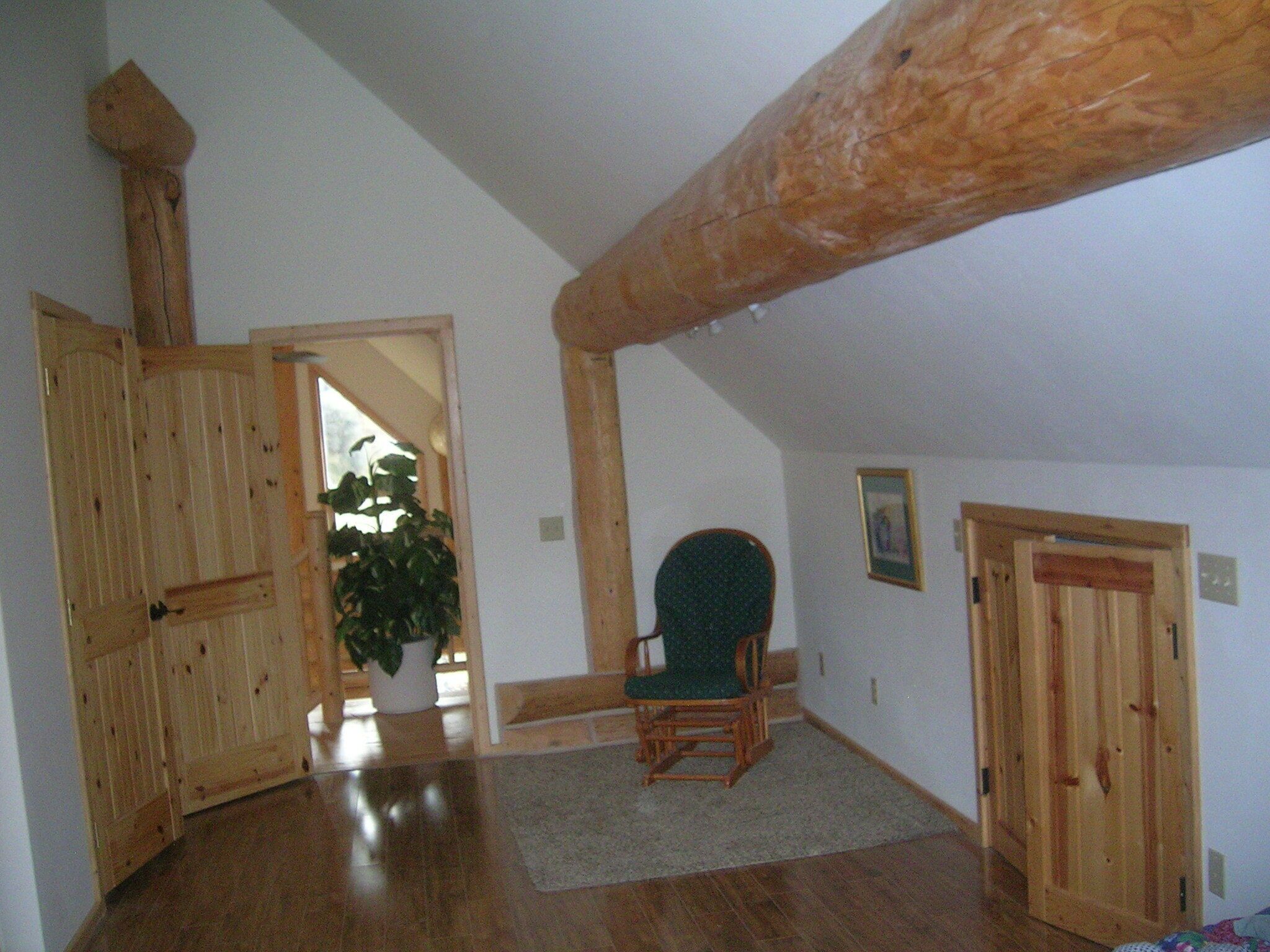 A spacious room with wooden floors, a green chair, and a door leading to another room.