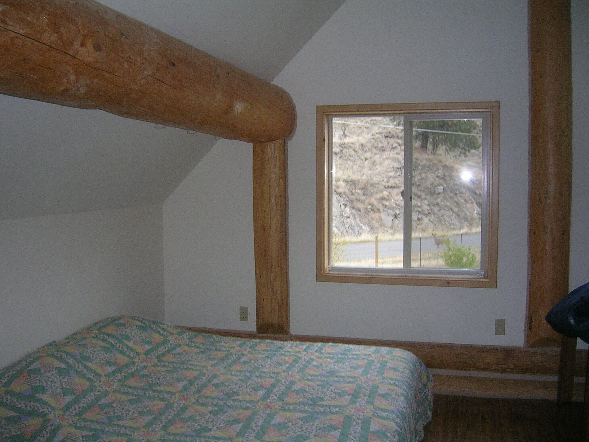 Un dormitorio con techo de madera, una ventana que da a un paisaje rocoso y una cama con colcha estampada.