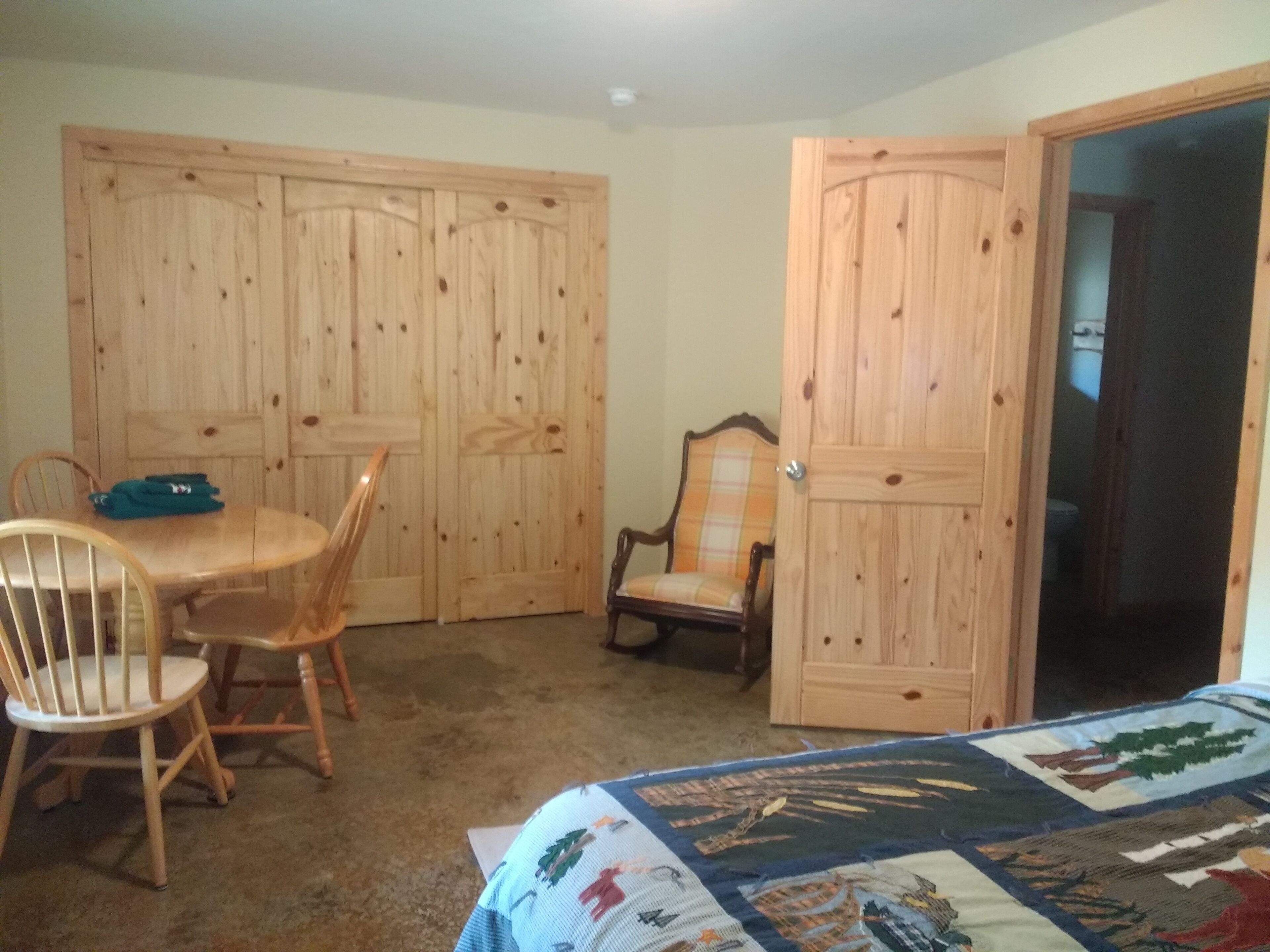 Ein Zimmer mit Holztisch und -stühlen, einer Bettdecke und Holzschränken.