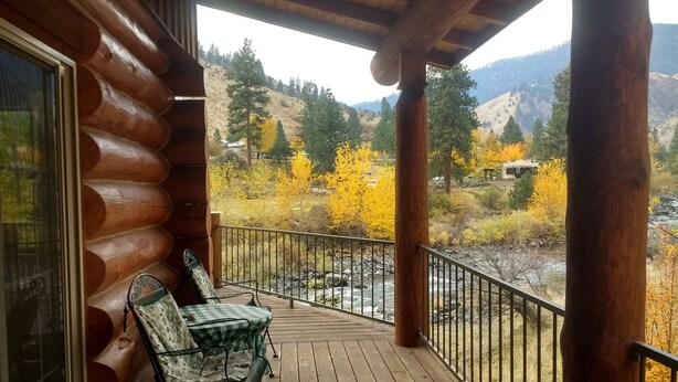 A wooden deck with a view of a river and autumn foliage. - Log cabin for salmon, fishing, hiking, cross-country skiing, 50 minutes to ski (Pollock)