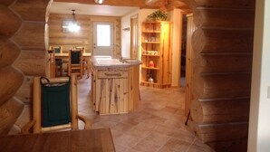 A wooden cabin interior with a kitchen area featuring a central island, a dining table, and a seating area with chairs. - Log cabin for salmon, fishing, hiking, cross-country skiing, 50 minutes to ski (Pollock)