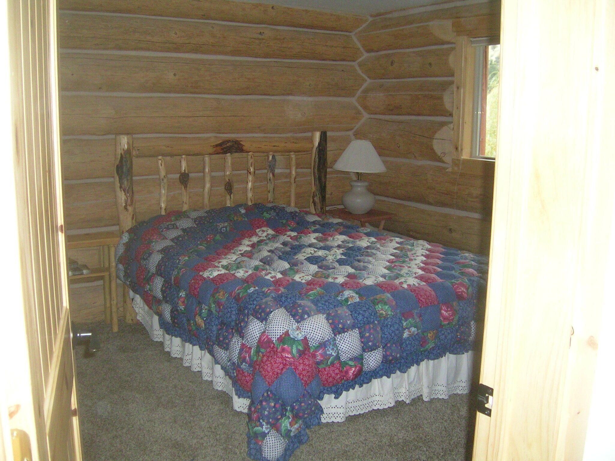 A log cabin bedroom with a bed, a lamp, and a window.