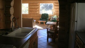 A cozy log cabin interior with a kitchen area featuring a sink, a dining table with chairs, and a green armchair by a window. - Log cabin for salmon, fishing, hiking, cross-country skiing, 50 minutes to ski (Pollock)