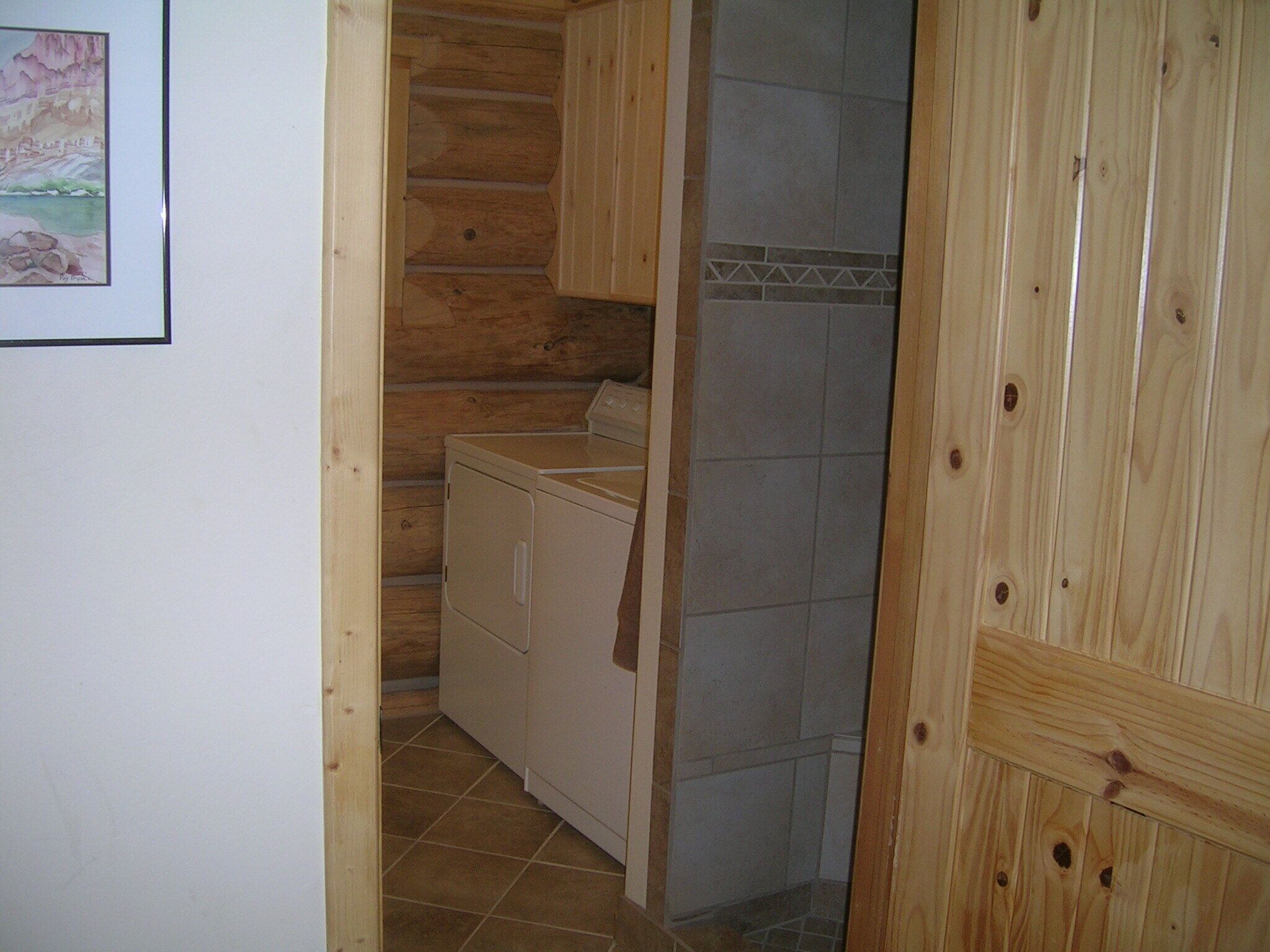 Un lavadero con lavadora, una zona de ducha con azulejos y paredes de madera.