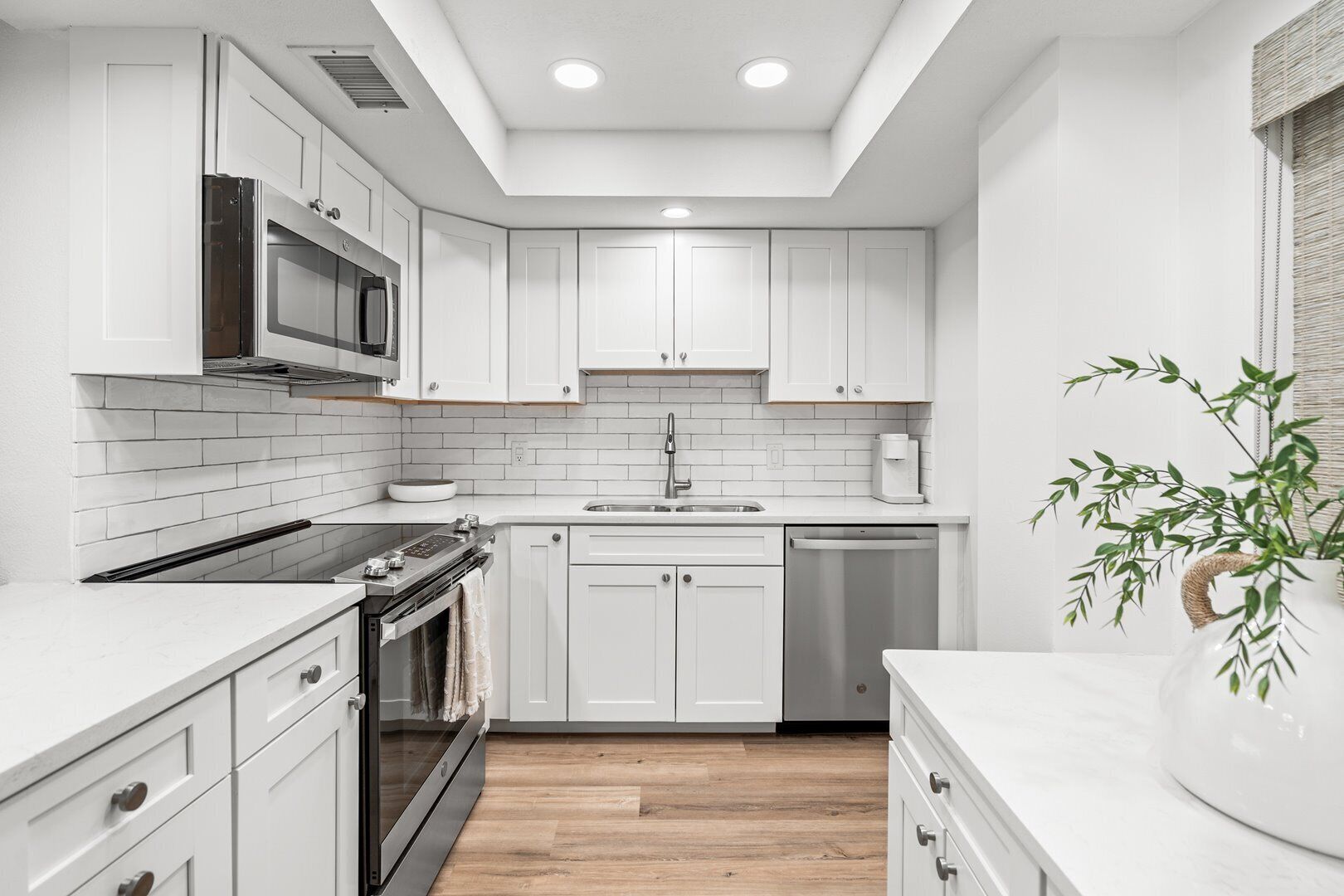A modern kitchen with white cabinets, a microwave, stove, sink, and dishwasher.