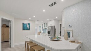 Una cocina moderna con una isla grande, armarios blancos y un refrigerador de acero inoxidable.