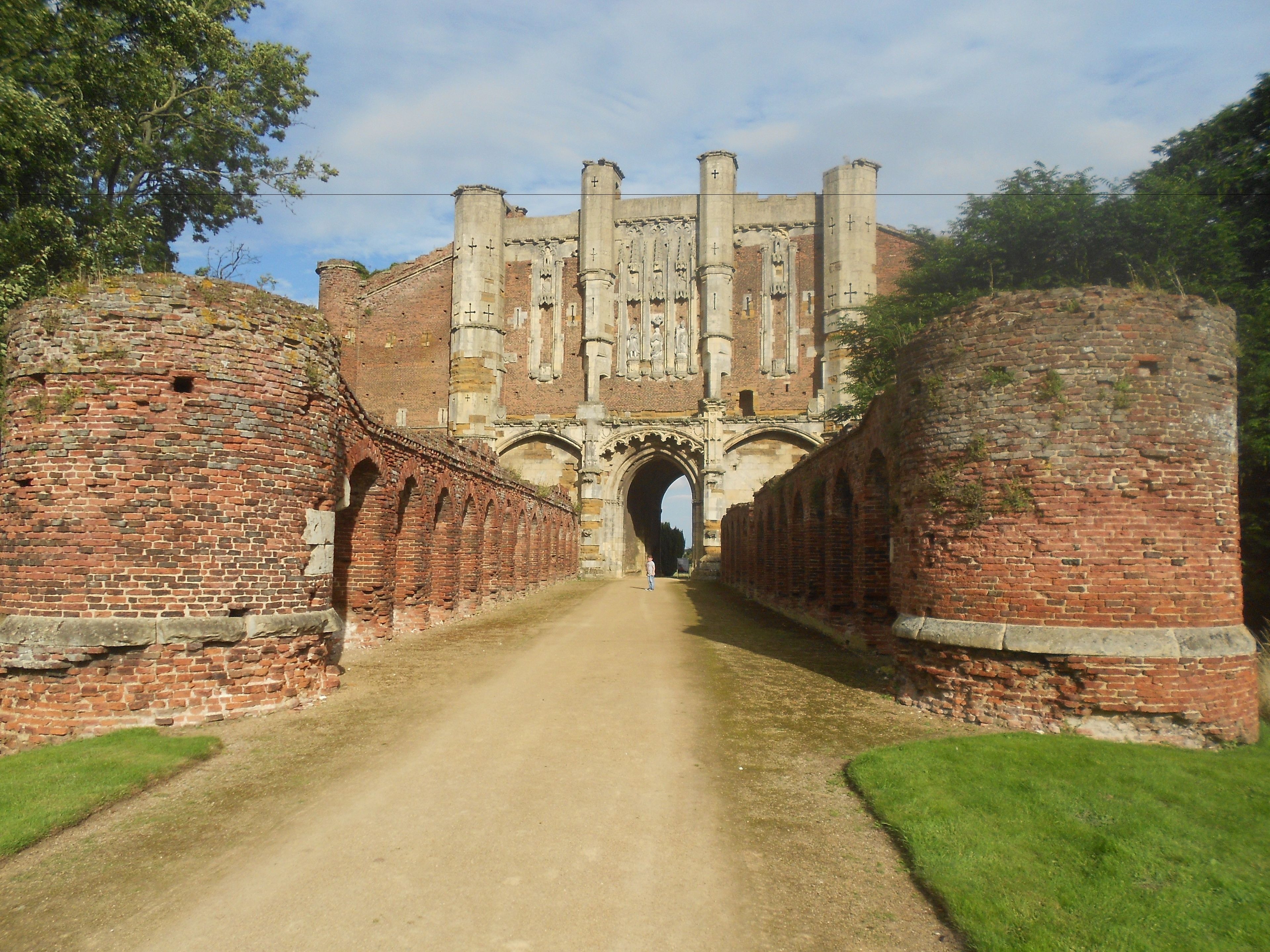 A historical building with a central archway, flanked by brick walls and a dirt path leading through.