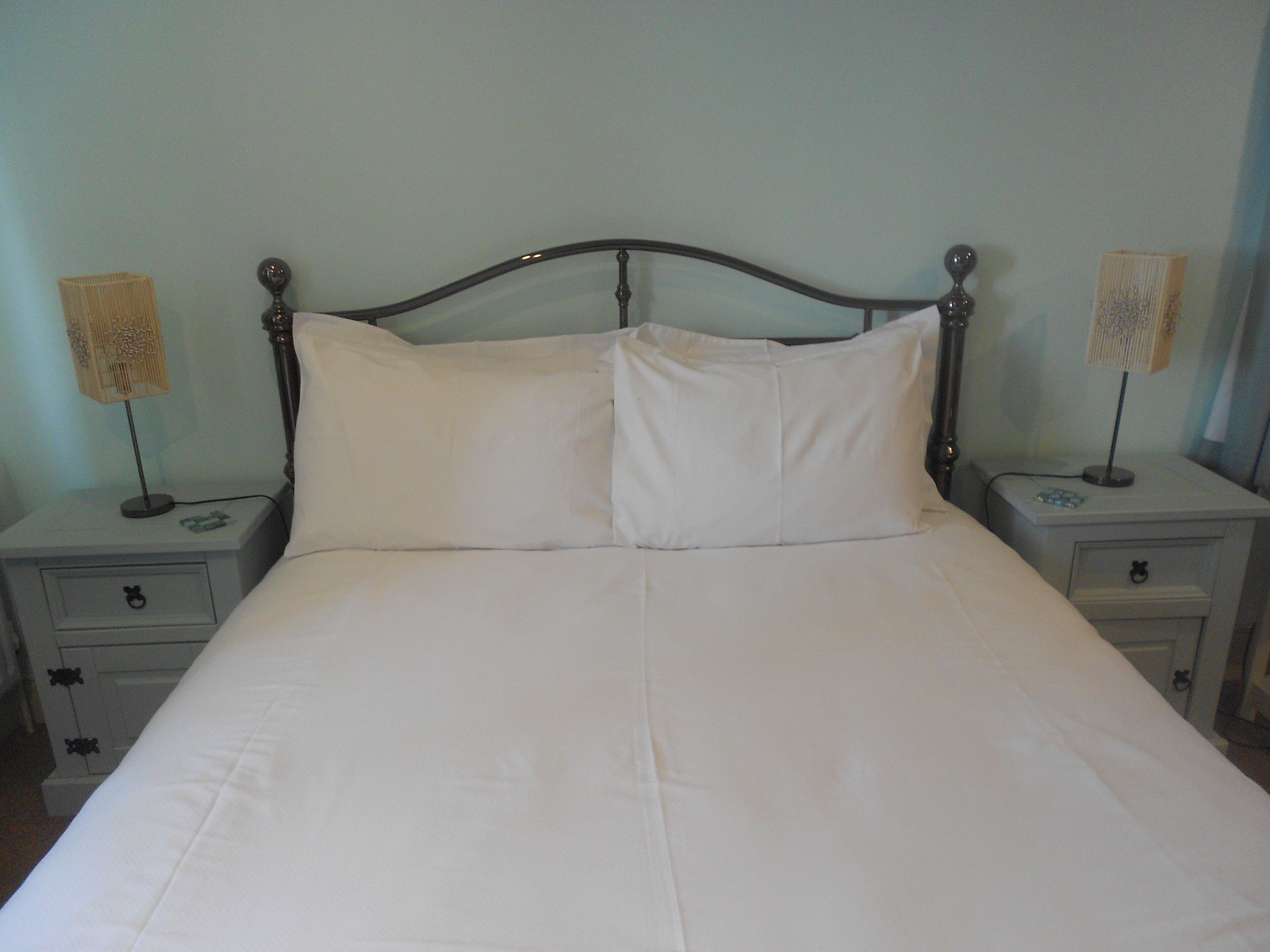 A bed with white linens, two bedside tables with lamps, and a nightstand drawer.