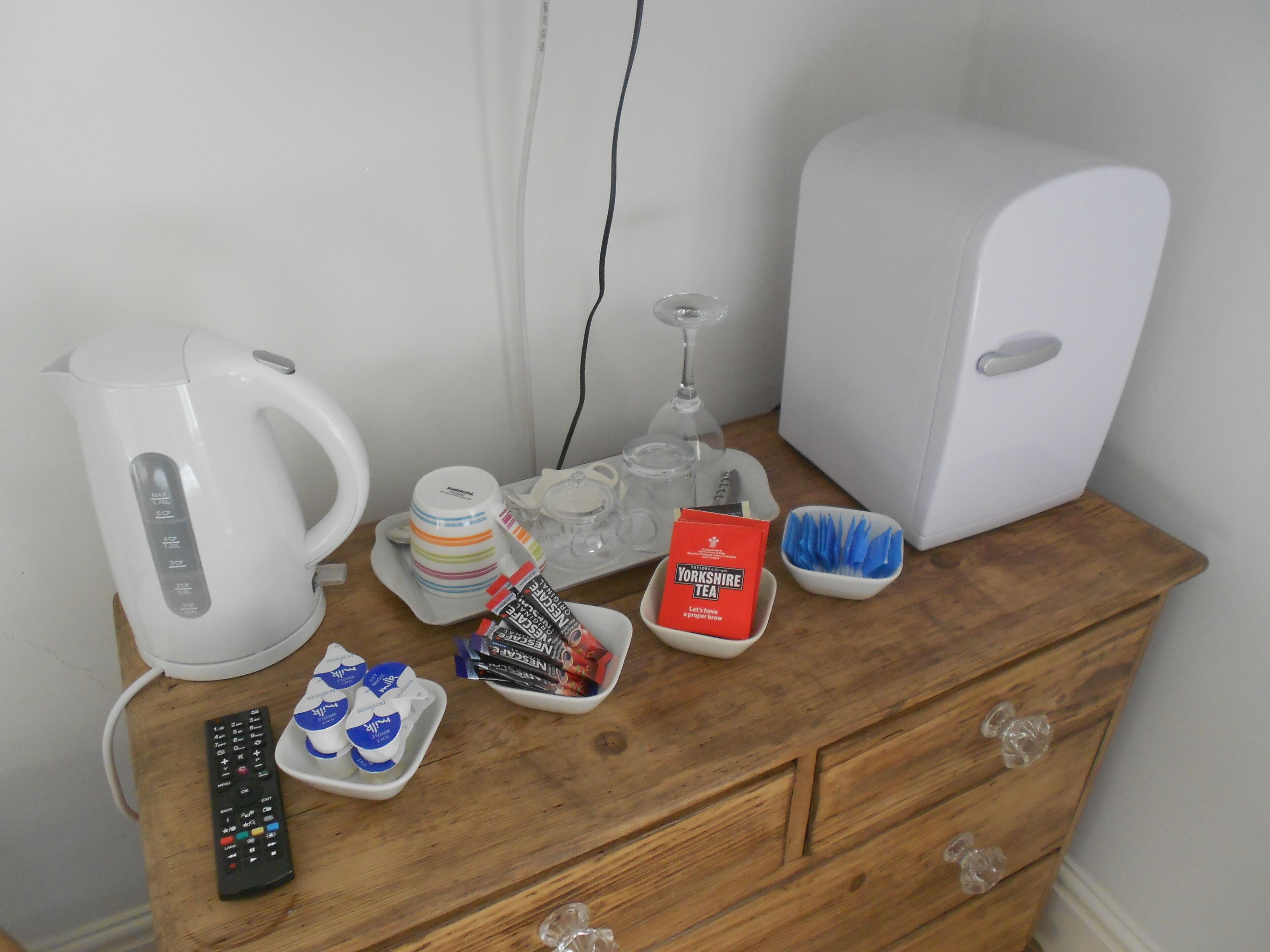 A wooden dresser with a white kettle, a glass, a wine glass, a remote control, and a box of Yorkshire tea.