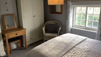 A bedroom with a bed, a wardrobe, a chair, a desk with a mirror, and a window with a view of trees.