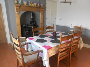 A dining area with a table set for six, surrounded by wooden chairs. A fireplace with a mantel is visible in the background.