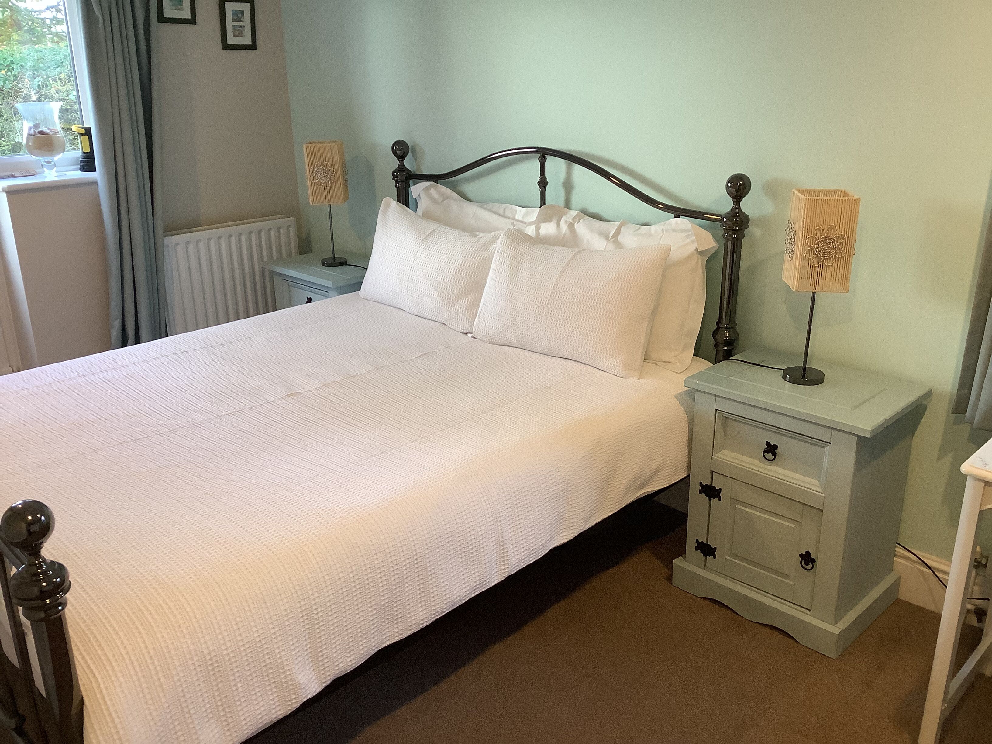 A neatly made bed with white linens, a wooden headboard, and a bedside table with a lamp.