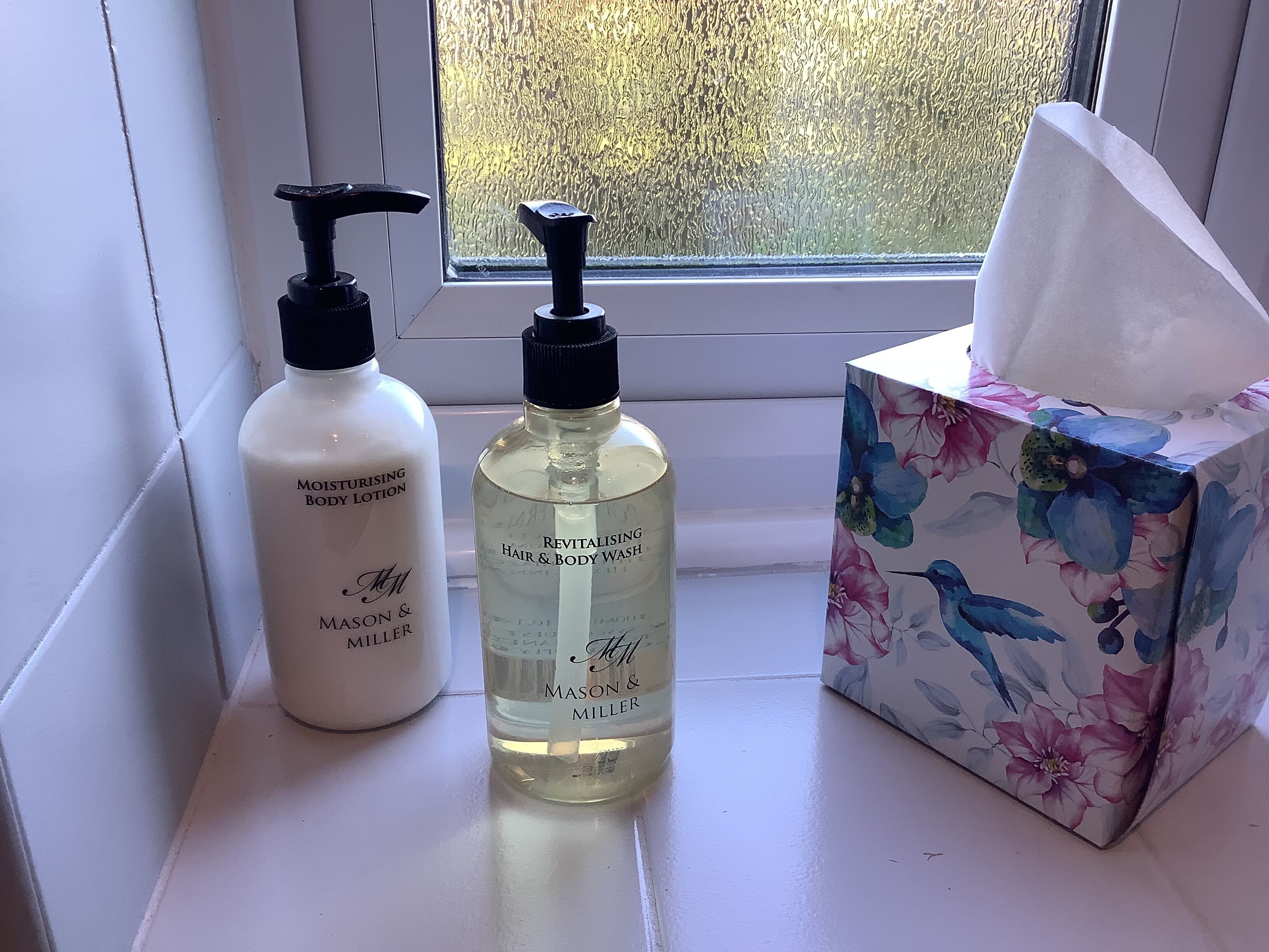 Two bottles of body lotion and a floral box on a windowsill.