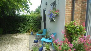 A small patio with two blue chairs, potted plants, and a gravel path leading to a building with a brick wall. - Villa Farm Cottage (Ulceby)