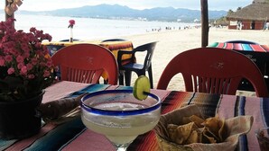 Ein Tisch am Strand mit einem Margarita, einer Topfpflanze und einer Snackkörbchen.