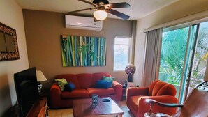 Ein Wohnzimmer mit einem roten Sofa, einem Holztisch, einem Ledersessel und einem Deckenventilator.
