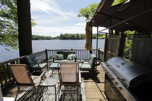 A deck with outdoor furniture, a grill, and a view of a lake.