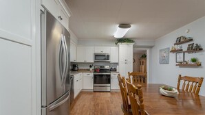 A modern kitchen with white cabinets, stainless steel appliances, a wooden dining table, and a view into the dining area. - Spacious 4BR getaway in downtown Brevard, perfect for family adventures! (Brevard)