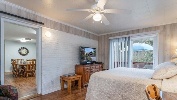 A bedroom with a bed, a television, a wooden dresser, a dining area with chairs, and a ceiling fan. - Spacious 4BR getaway in downtown Brevard, perfect for family adventures! (Brevard)
