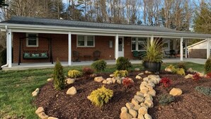 A brick house with a covered porch, a small garden with rocks and shrubs, and a lawn. - Spacious 4BR getaway in downtown Brevard, perfect for family adventures! (Brevard)