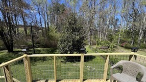 A wooden deck with a metal railing, a plastic chair, and a view of a wooded area. - Spacious 4BR getaway in downtown Brevard, perfect for family adventures! (Brevard)