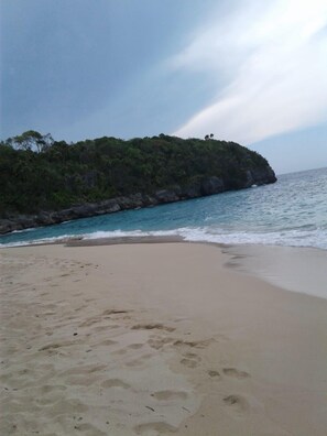 Una playa con arena, un promontorio rocoso y mar tranquilo.