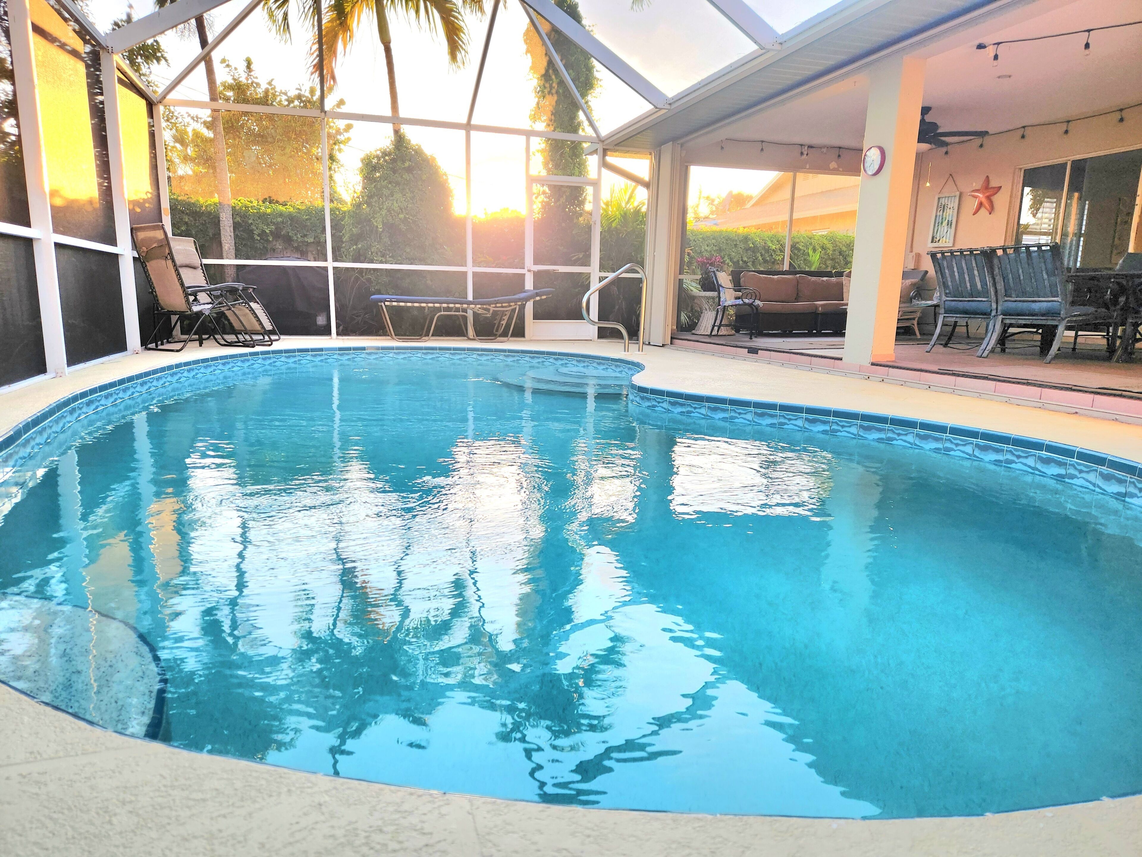 A clear swimming pool with lounge chairs and a covered patio area.