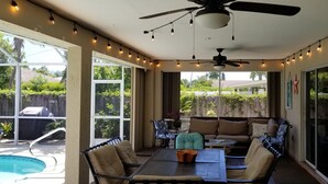 Eine Außenpatio mit Pool, Deckenventilator, Lichterkette und einer Sitzgruppe mit Tisch und Stühlen.